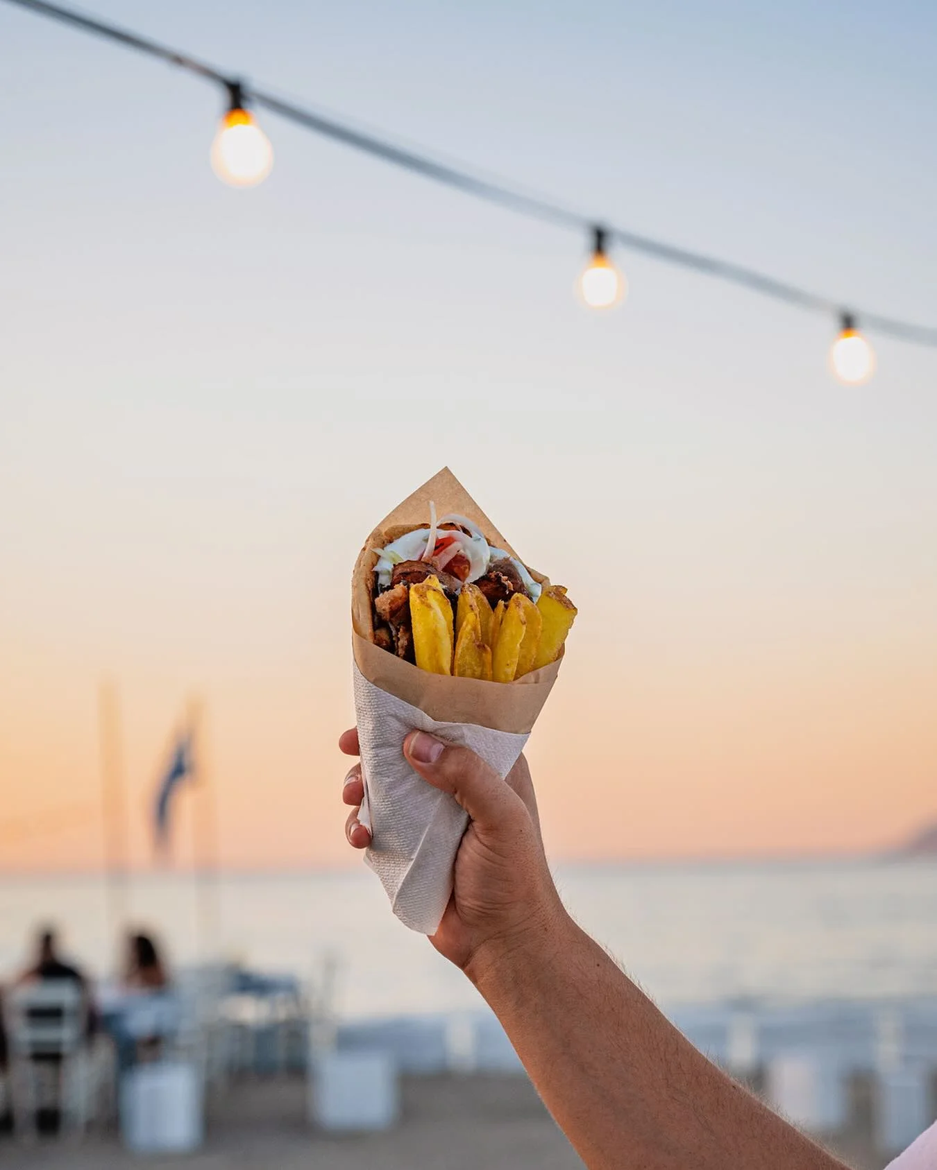 Pork gyros pita with fries held against a Kissamos sunset